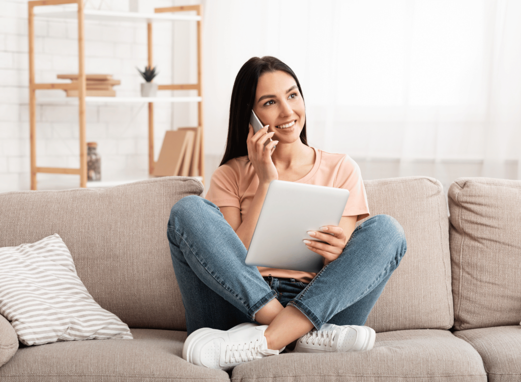 Woman sitting on couch talking on mobile phone and holding tablet