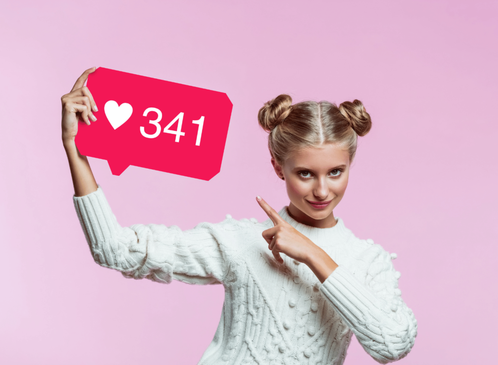 Woman wearing white jumper and smiling and pointing at 341 heart notifications against pink background