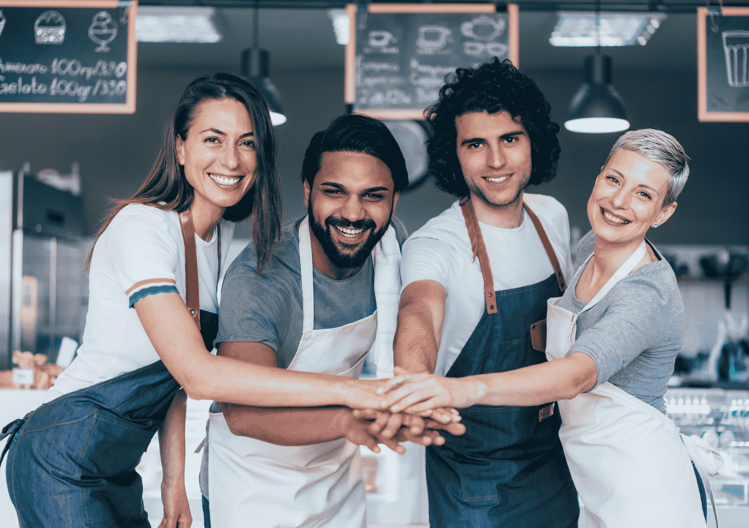 Small team of happy men and women wearing aprons in a cafe placing hands together
